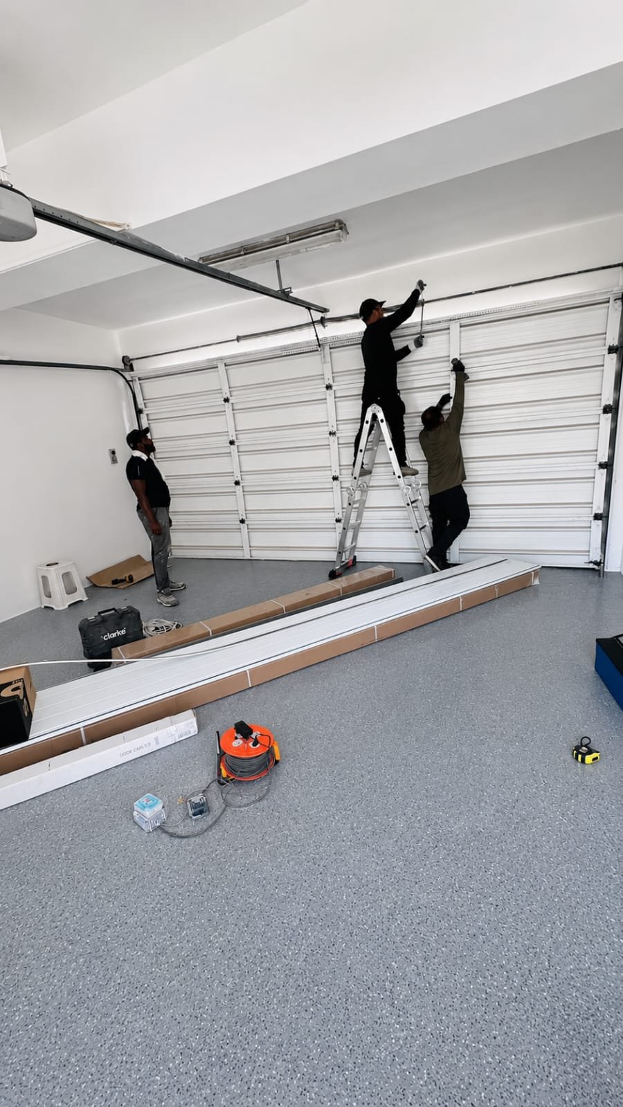 Three technicians installing white sectional garage door at Dubai villa